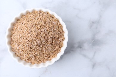 Photo of Buckwheat bran in bowl on white marble table, top view. Space for text