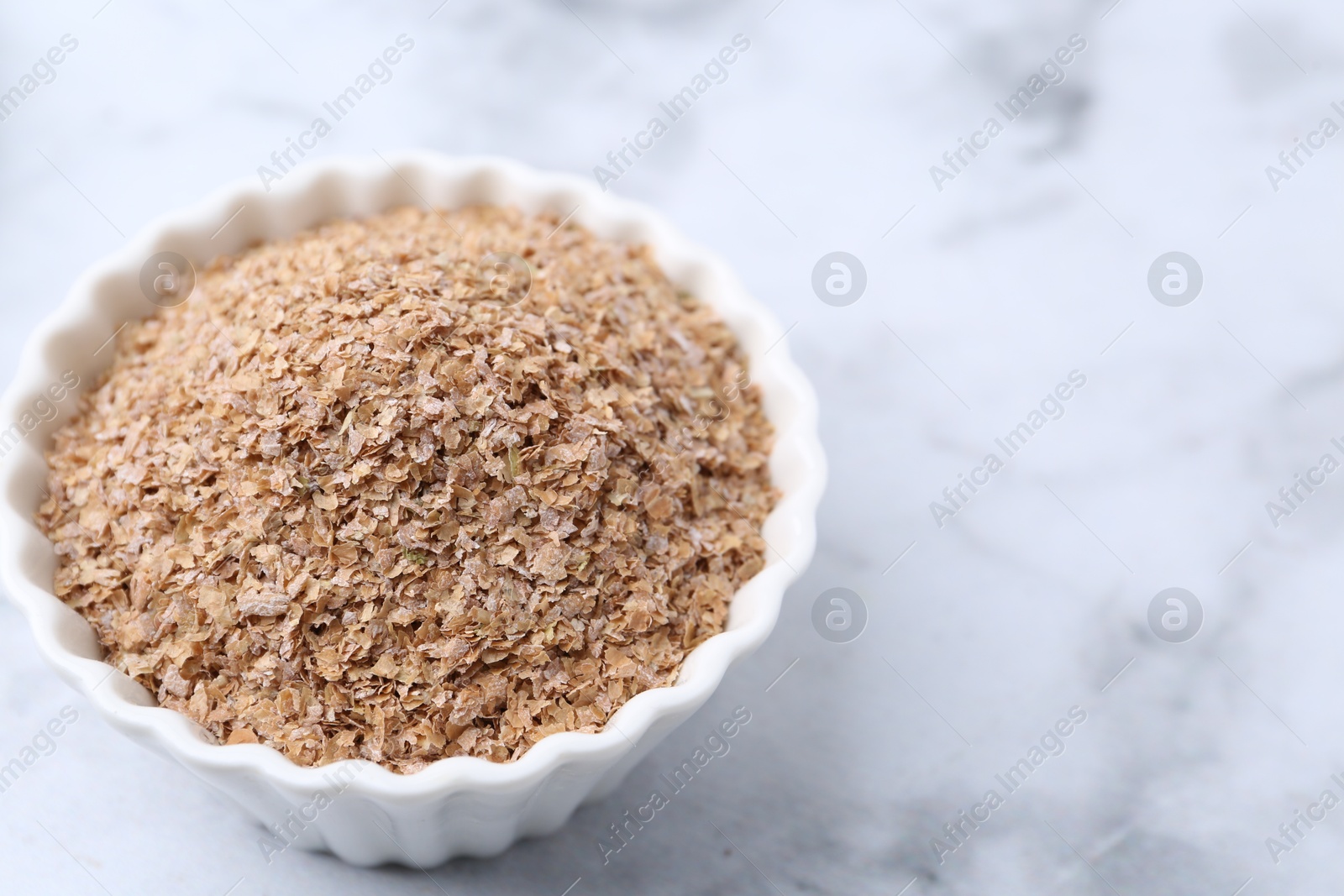 Photo of Buckwheat bran in bowl on white marble table, closeup. Space for text