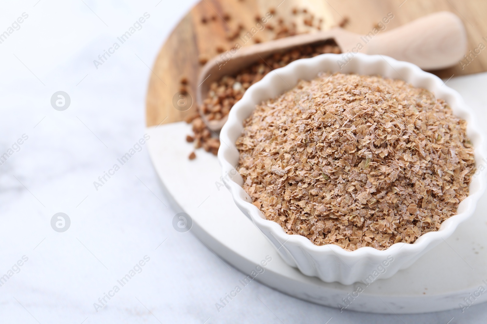 Photo of Buckwheat bran in bowl on white marble table, closeup. Space for text