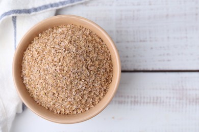 Buckwheat bran in bowl on white wooden table, top view. Space for text