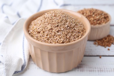 Photo of Buckwheat bran in bowl on white wooden table, closeup