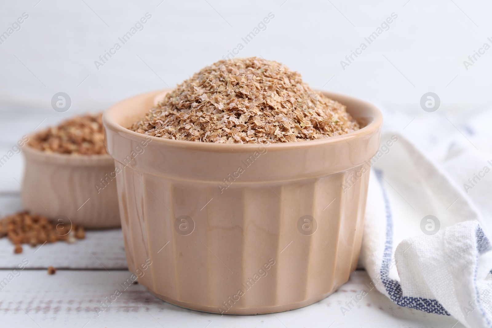 Photo of Buckwheat bran in bowl on white wooden table, closeup