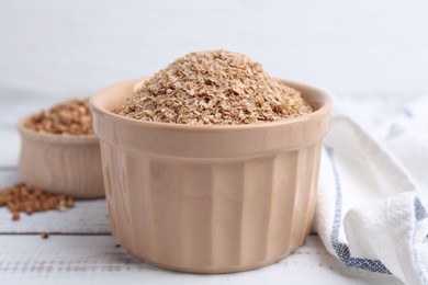 Photo of Buckwheat bran in bowl on white wooden table, closeup