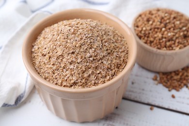 Photo of Buckwheat bran in bowl on white wooden table, closeup