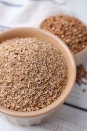 Buckwheat bran in bowl on white wooden table, closeup