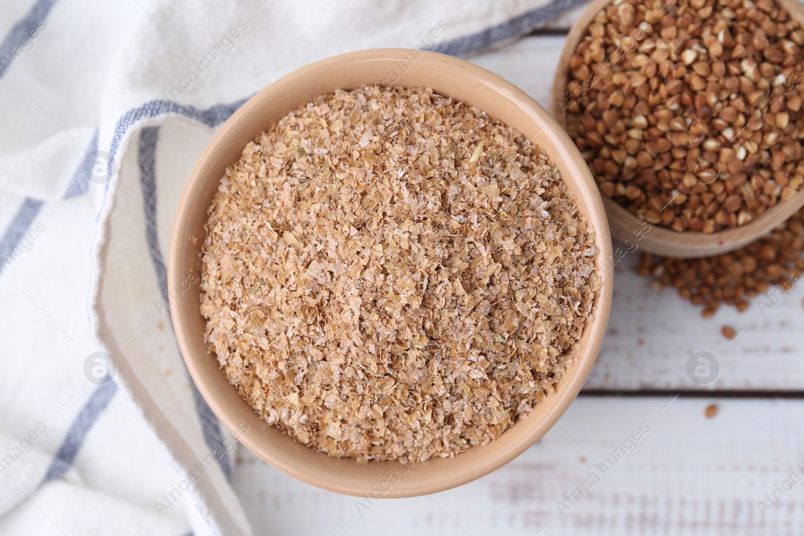 Photo of Buckwheat bran in bowl and grains on white wooden table, top view