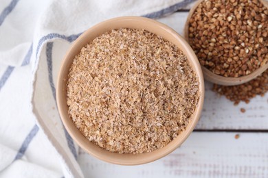 Photo of Buckwheat bran in bowl and grains on white wooden table, top view