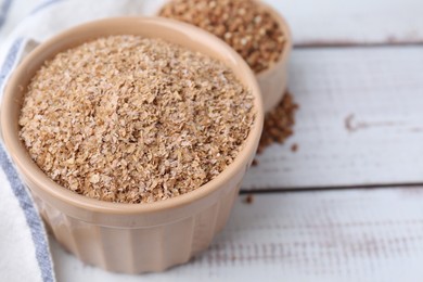 Photo of Buckwheat bran in bowl on white wooden table, closeup. Space for text