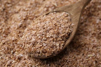 Photo of Pile of buckwheat bran and wooden spoon, closeup