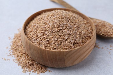 Photo of Buckwheat bran in bowl and spoon on light grey table, closeup