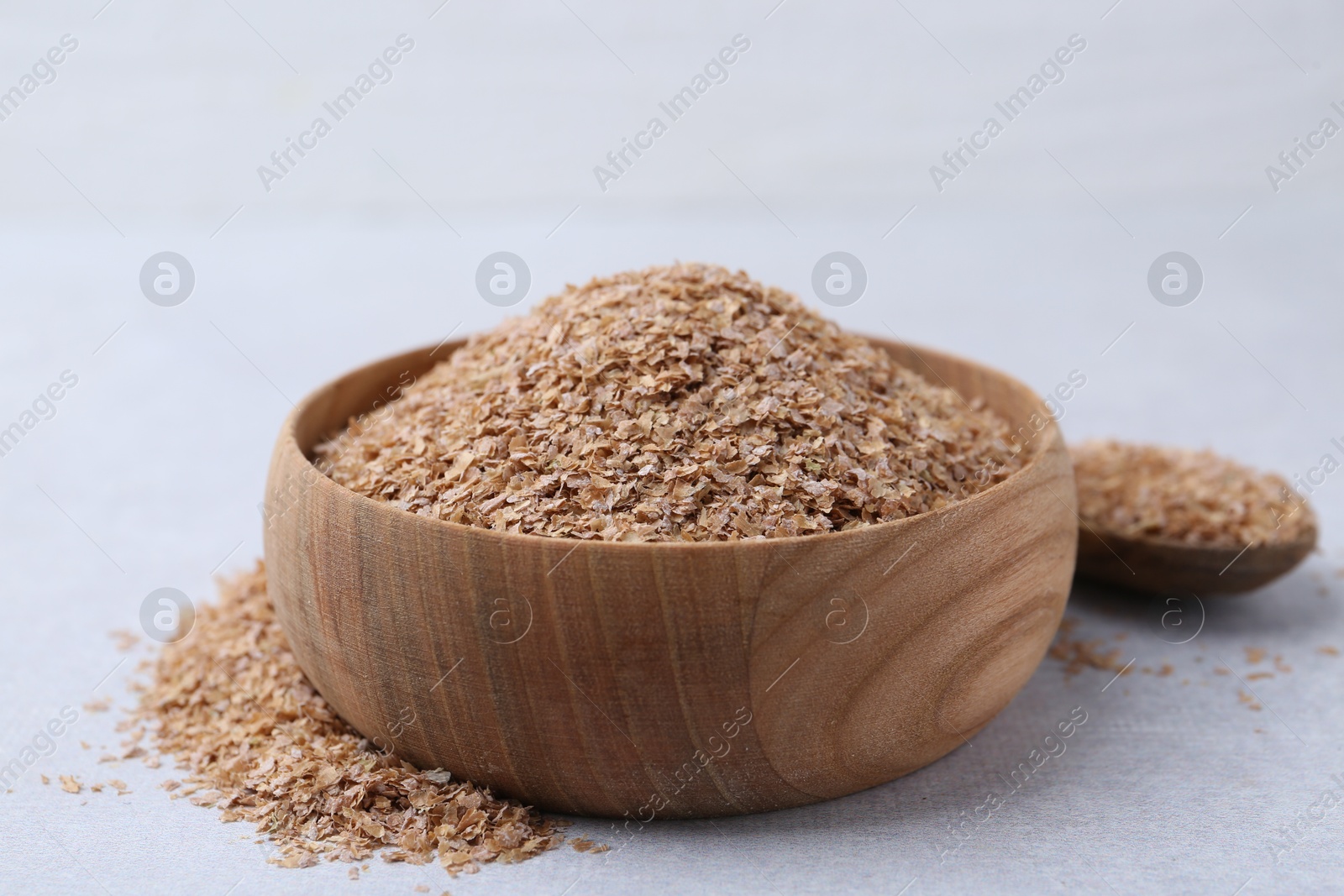 Photo of Buckwheat bran in bowl and spoon on light grey table, closeup