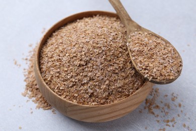 Photo of Buckwheat bran in bowl and spoon on light grey table, closeup