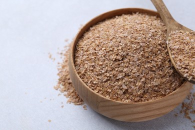 Photo of Buckwheat bran in bowl and spoon on light grey table, closeup. Space for text