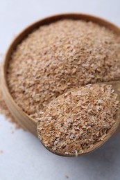 Photo of Buckwheat bran in bowl and spoon on light grey table, closeup