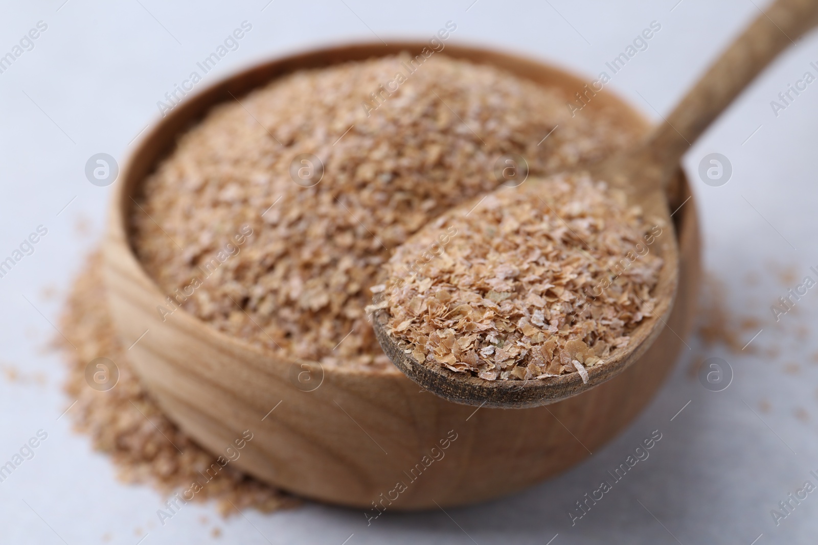 Photo of Buckwheat bran in bowl and spoon on light grey table, closeup