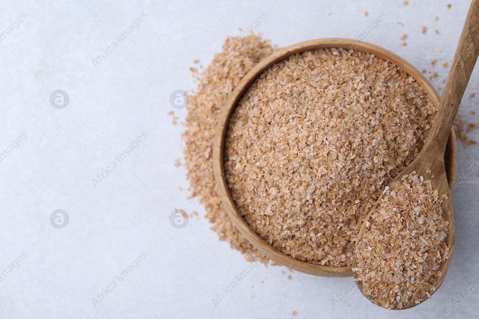 Photo of Buckwheat bran in bowl and spoon on light grey table, top view. Space for text