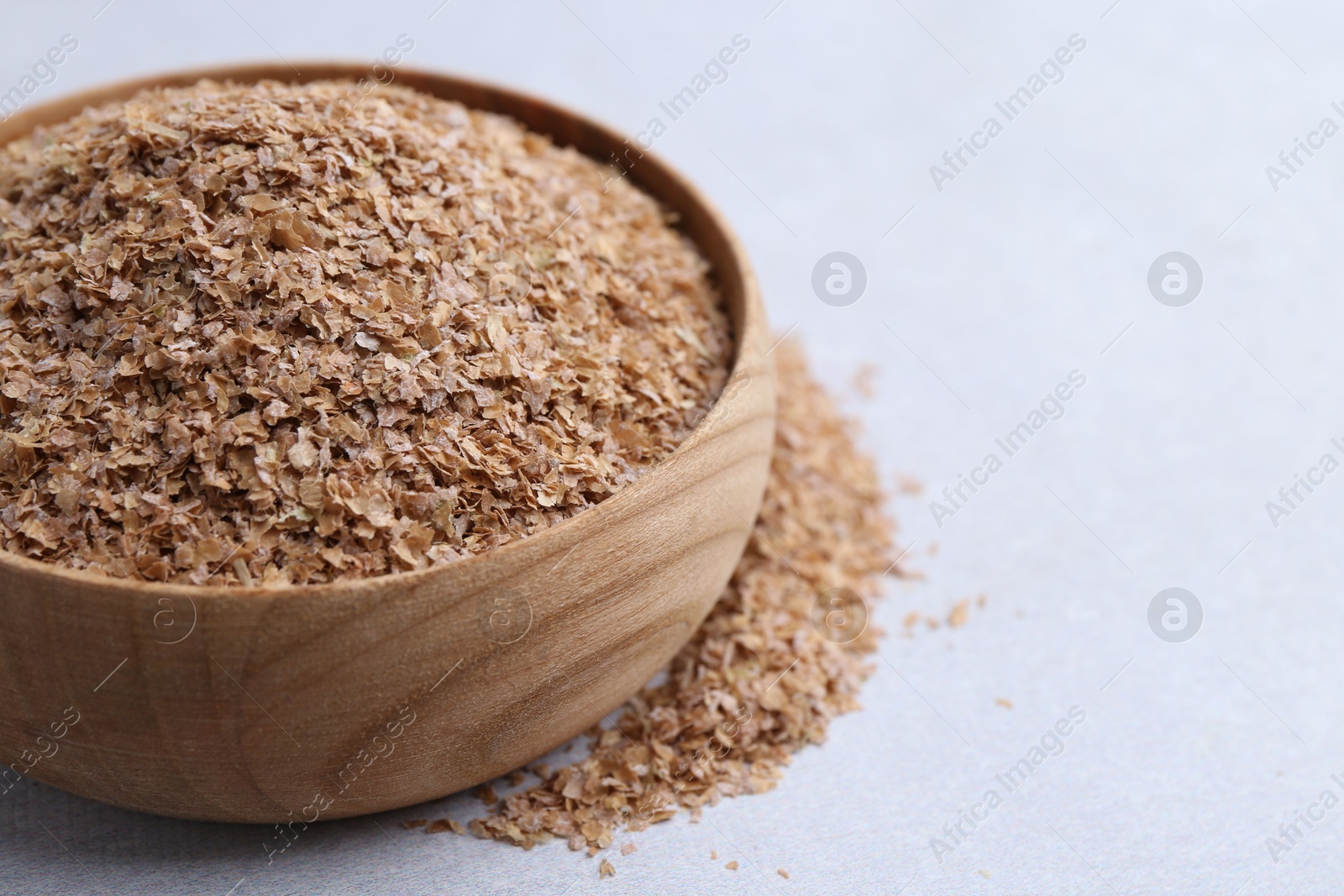 Photo of Buckwheat bran in bowl on light grey table, closeup. Space for text