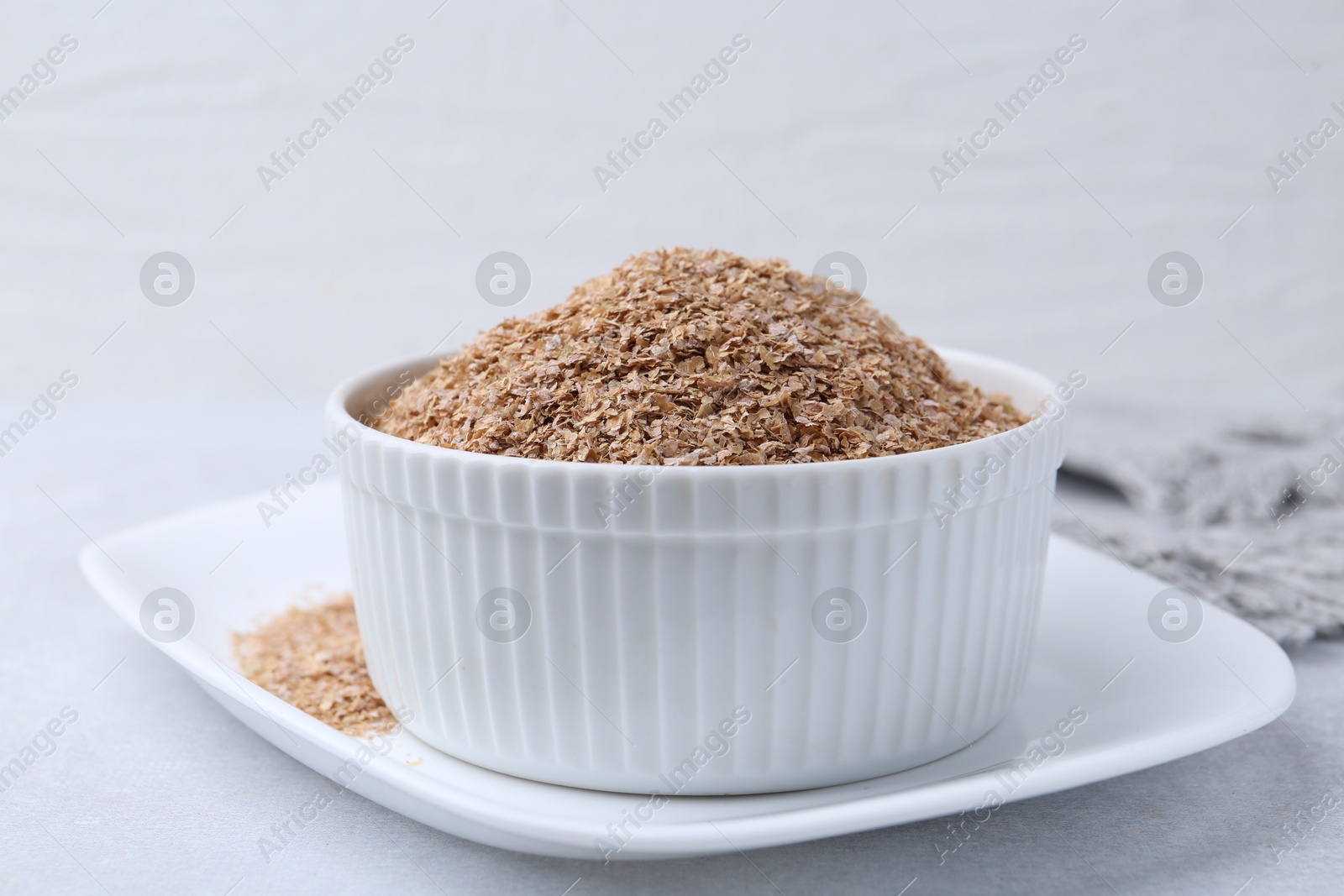 Photo of Buckwheat bran in bowl on light grey table, closeup