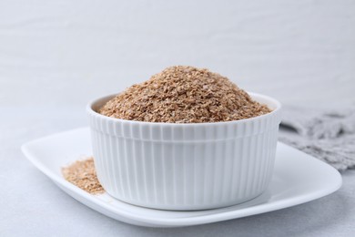 Buckwheat bran in bowl on light grey table, closeup