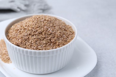 Buckwheat bran in bowl on light grey table, closeup