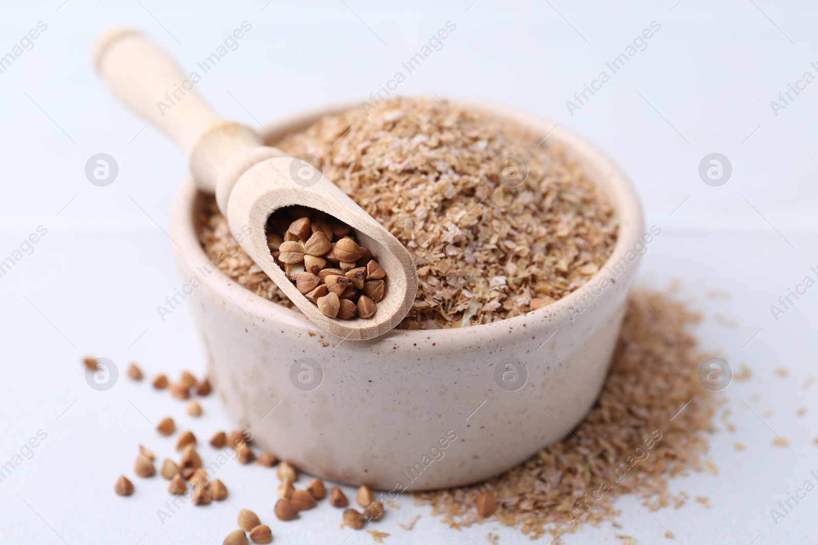 Photo of Buckwheat bran in bowl and grains on white table, closeup