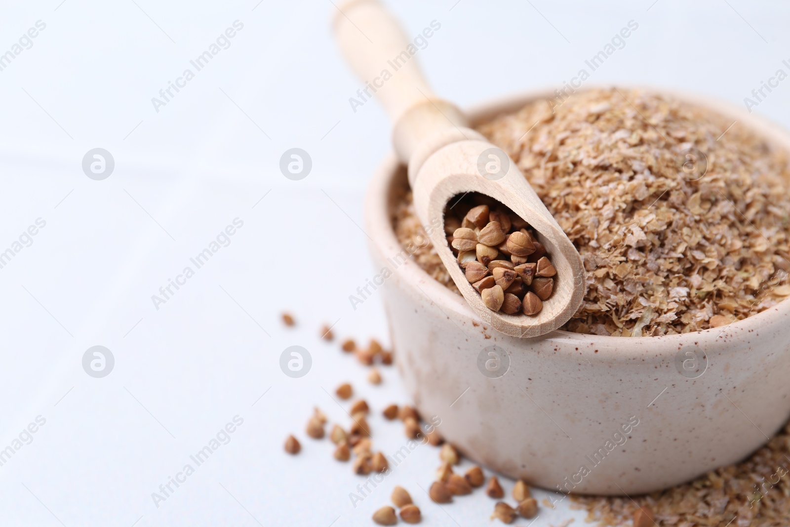 Photo of Buckwheat bran in bowl and grains on white table, closeup. Space for text