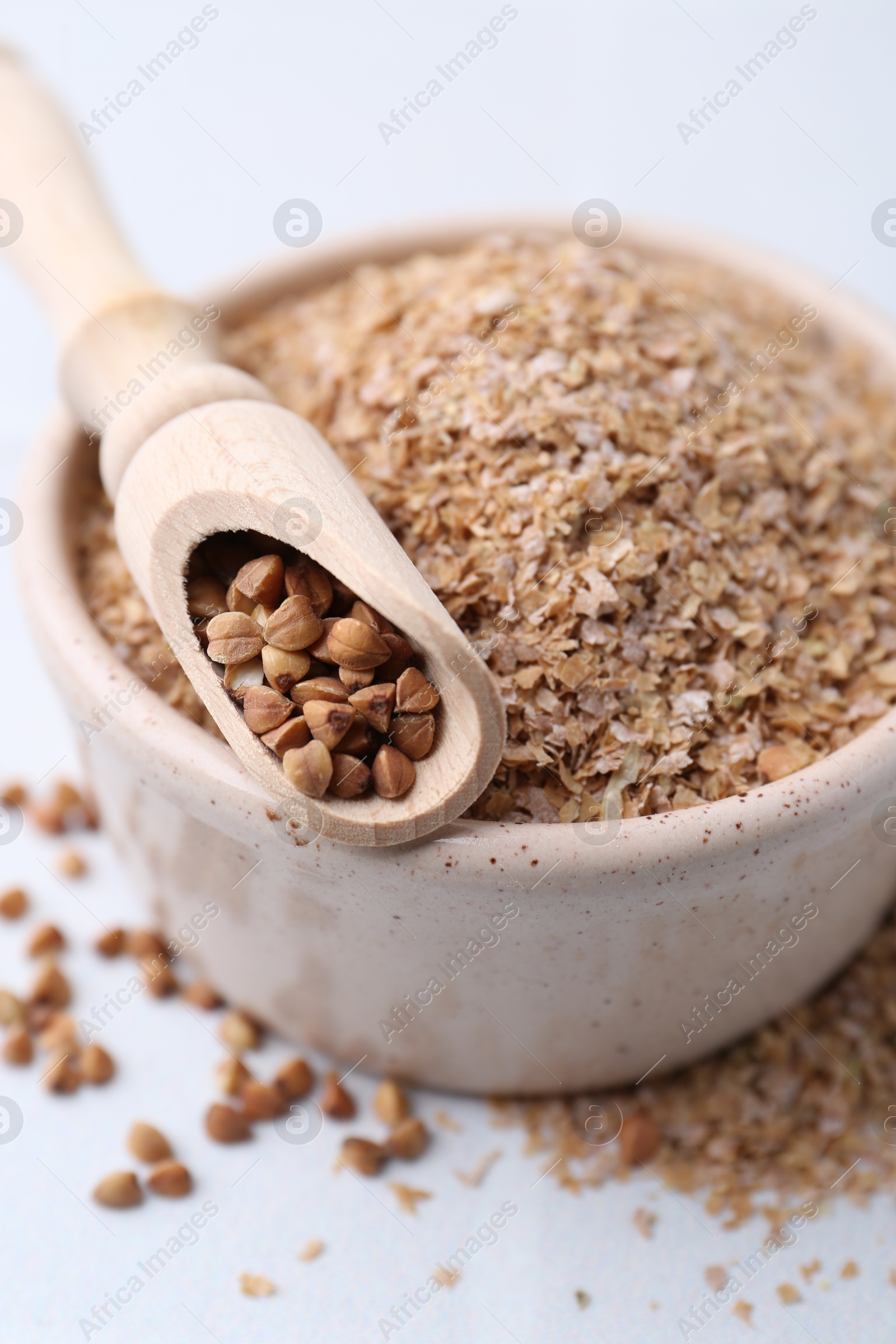 Photo of Buckwheat bran in bowl and grains on white table, closeup