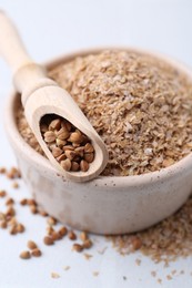 Photo of Buckwheat bran in bowl and grains on white table, closeup