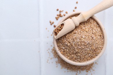 Photo of Buckwheat bran in bowl and grains on white table, top view. Space for text