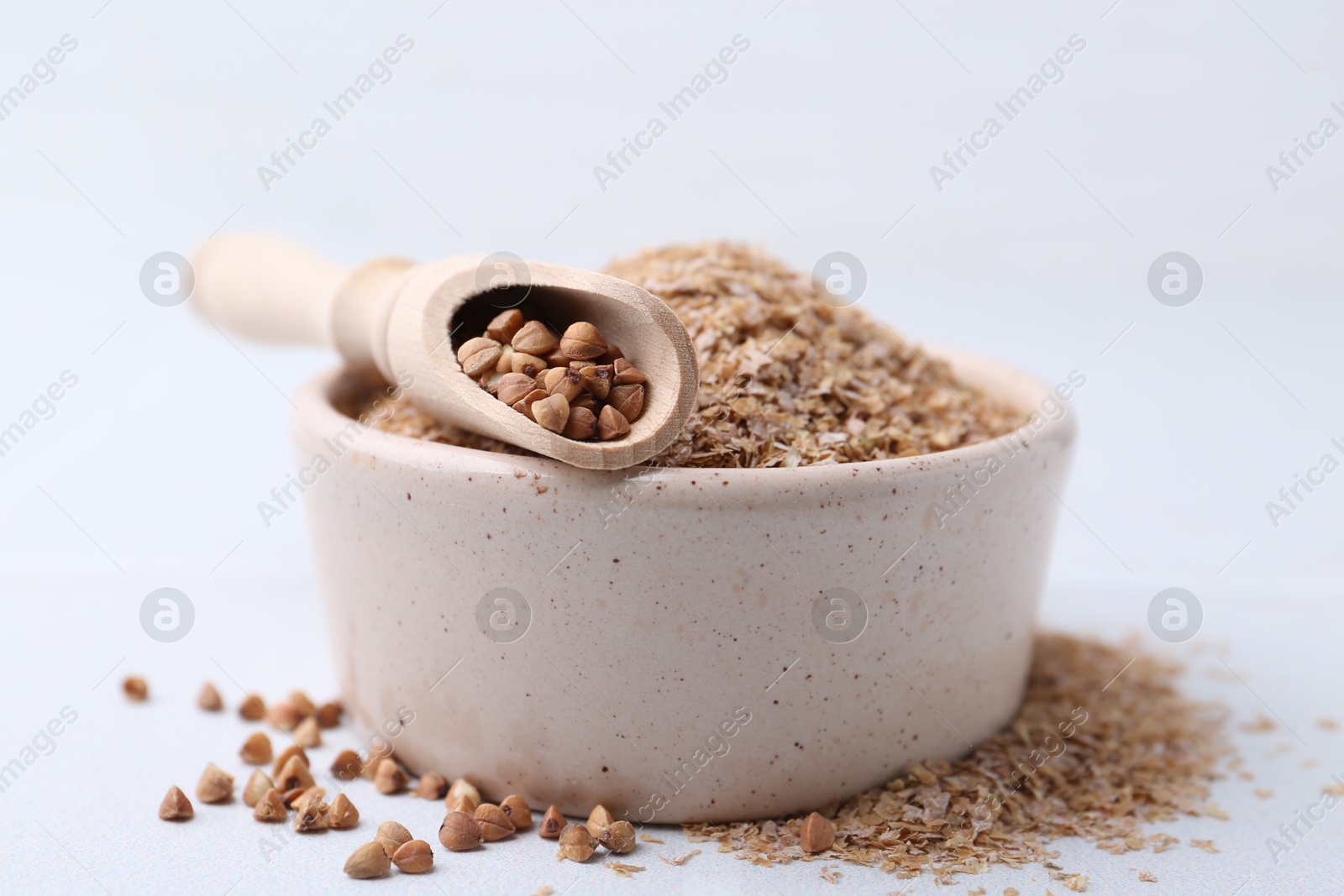 Photo of Buckwheat bran in bowl and grains on white table, closeup