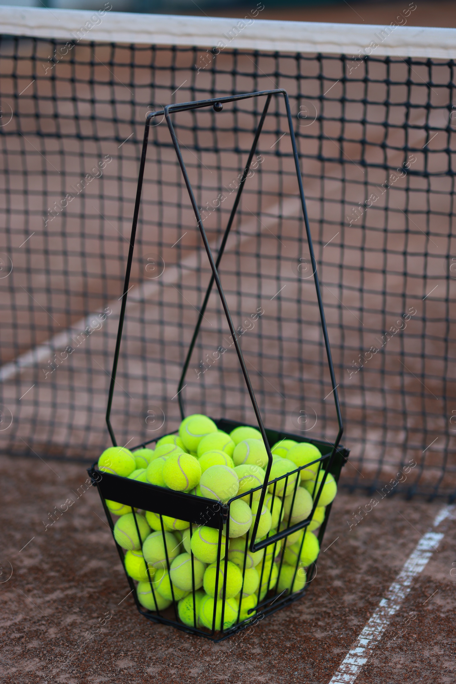 Photo of Many tennis balls in metal basket on court