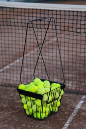 Many tennis balls in metal basket on court