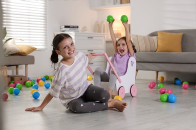 Cute little sisters playing with wooden stroller at home