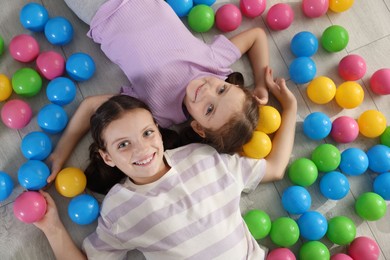 Photo of Cute little sisters playing with colorful balls on floor at home, top view