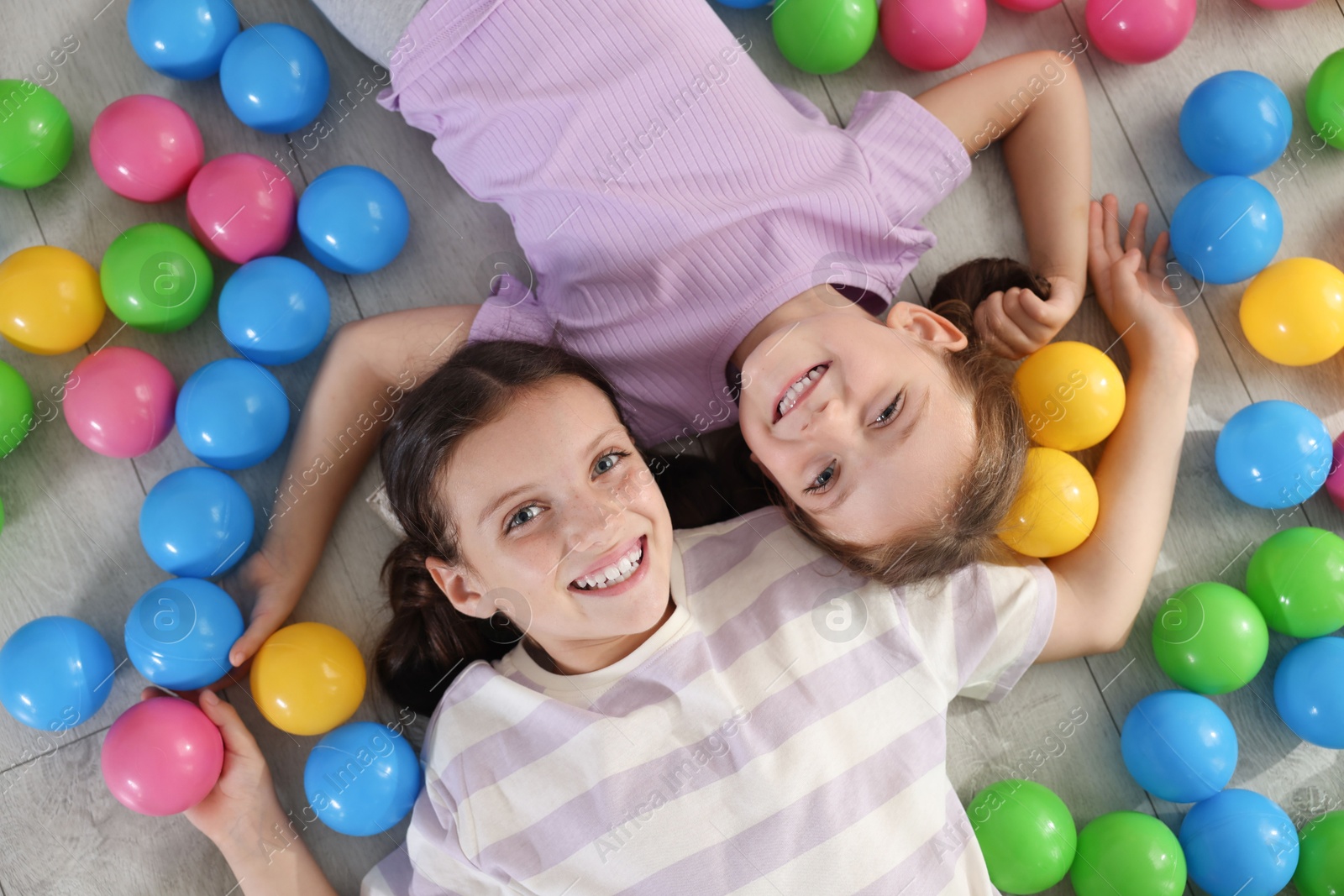 Photo of Cute little sisters playing with colorful balls on floor at home, top view