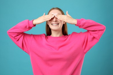 Photo of Smiling girl with braces covering eyes on light blue background