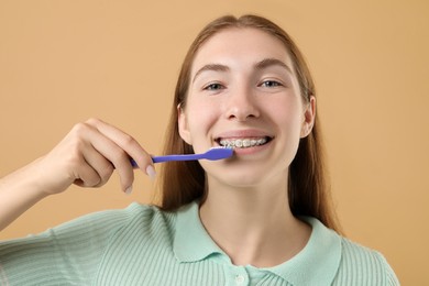 Photo of Girl with braces cleaning teeth on beige background