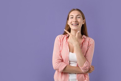 Photo of Smiling girl with braces on purple background, space for text