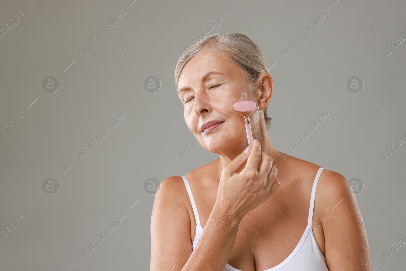 Photo of Beautiful woman doing facial massage with roller on grey background