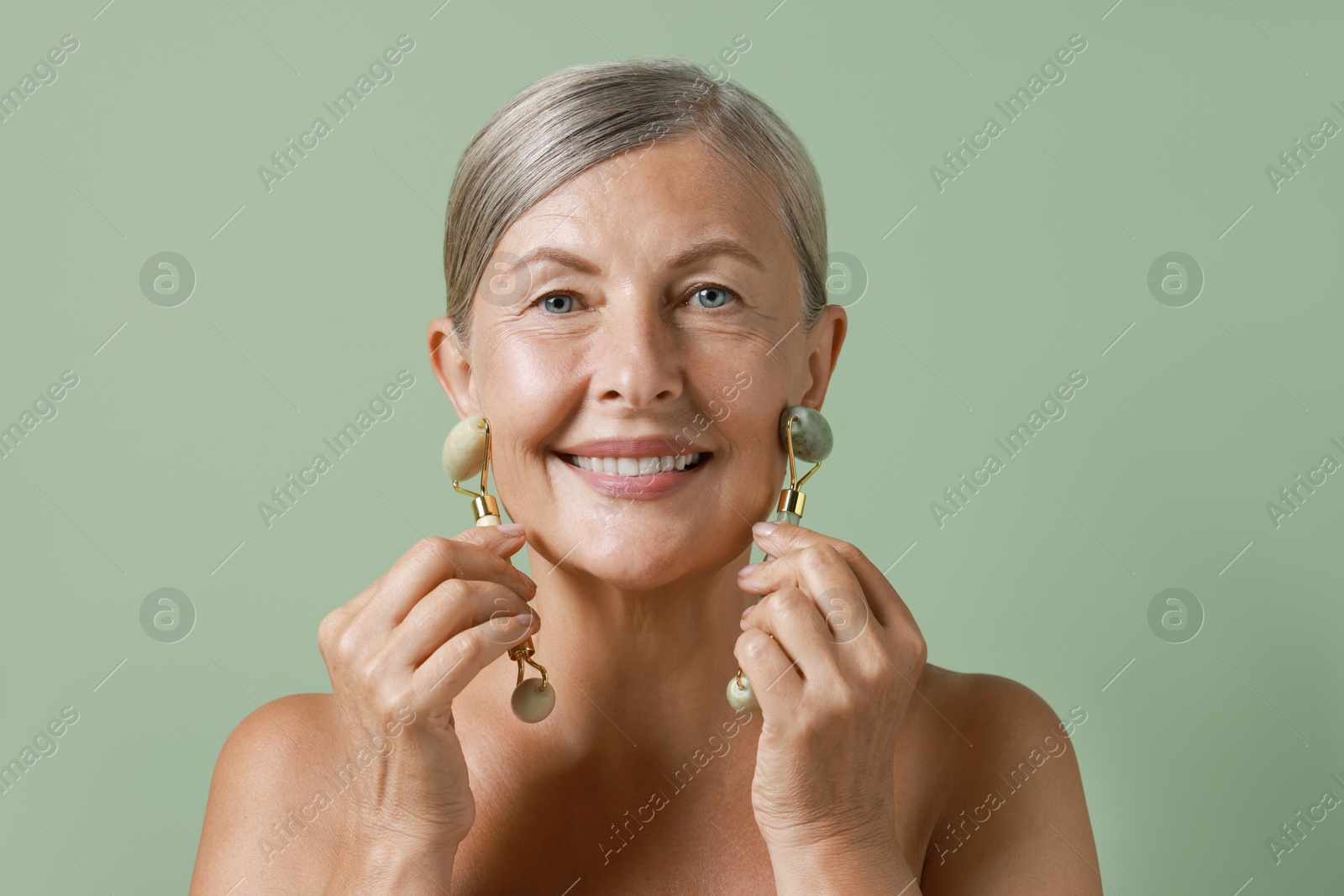 Photo of Beautiful woman doing facial massage with rollers on light green background