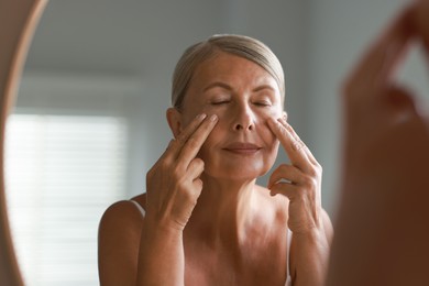 Beautiful woman doing facial massage near mirror at home