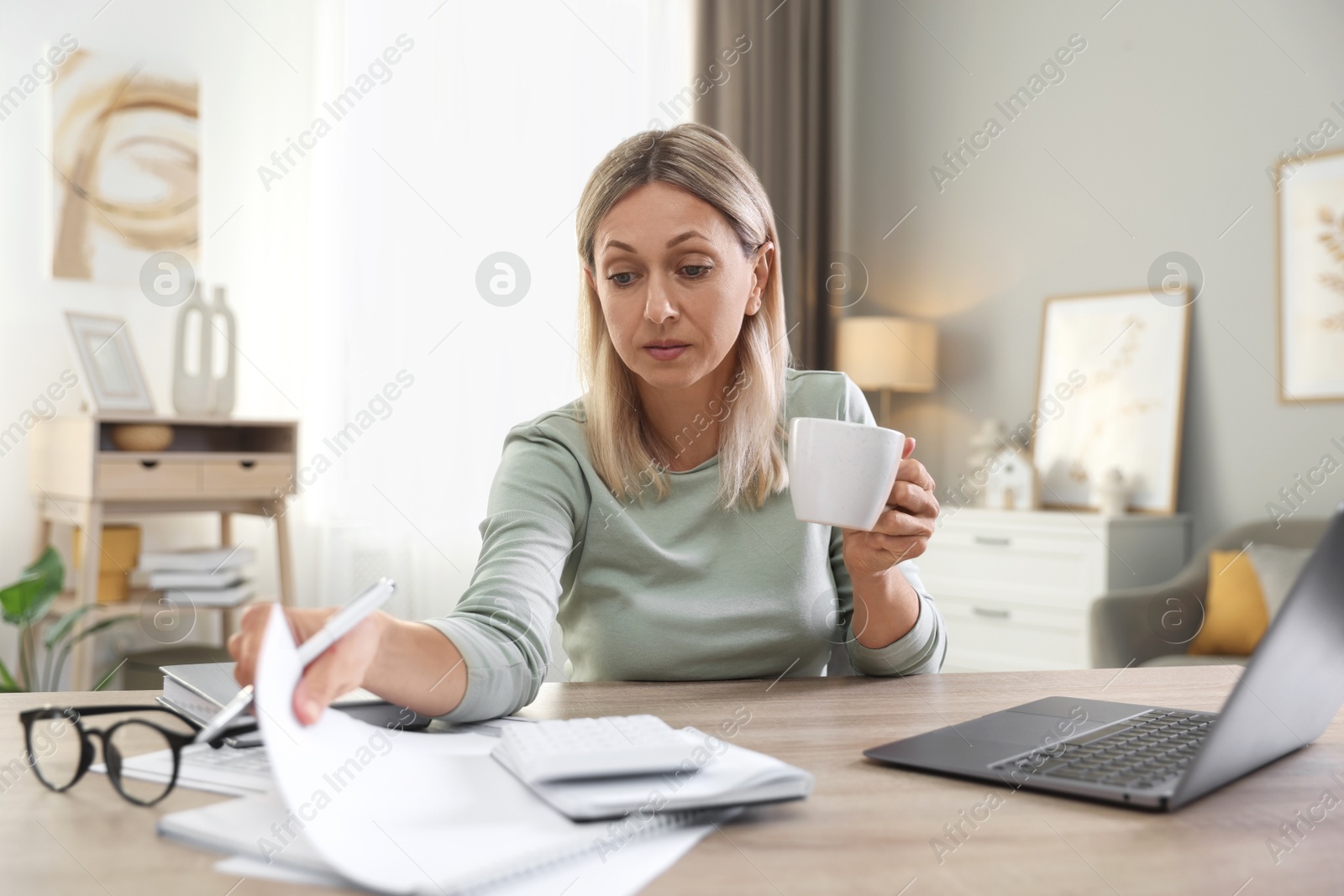 Photo of Budget planning. Woman with cup of drink and document at table indoors