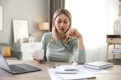 Budget planning. Woman with glasses and cup of drink at table indoors