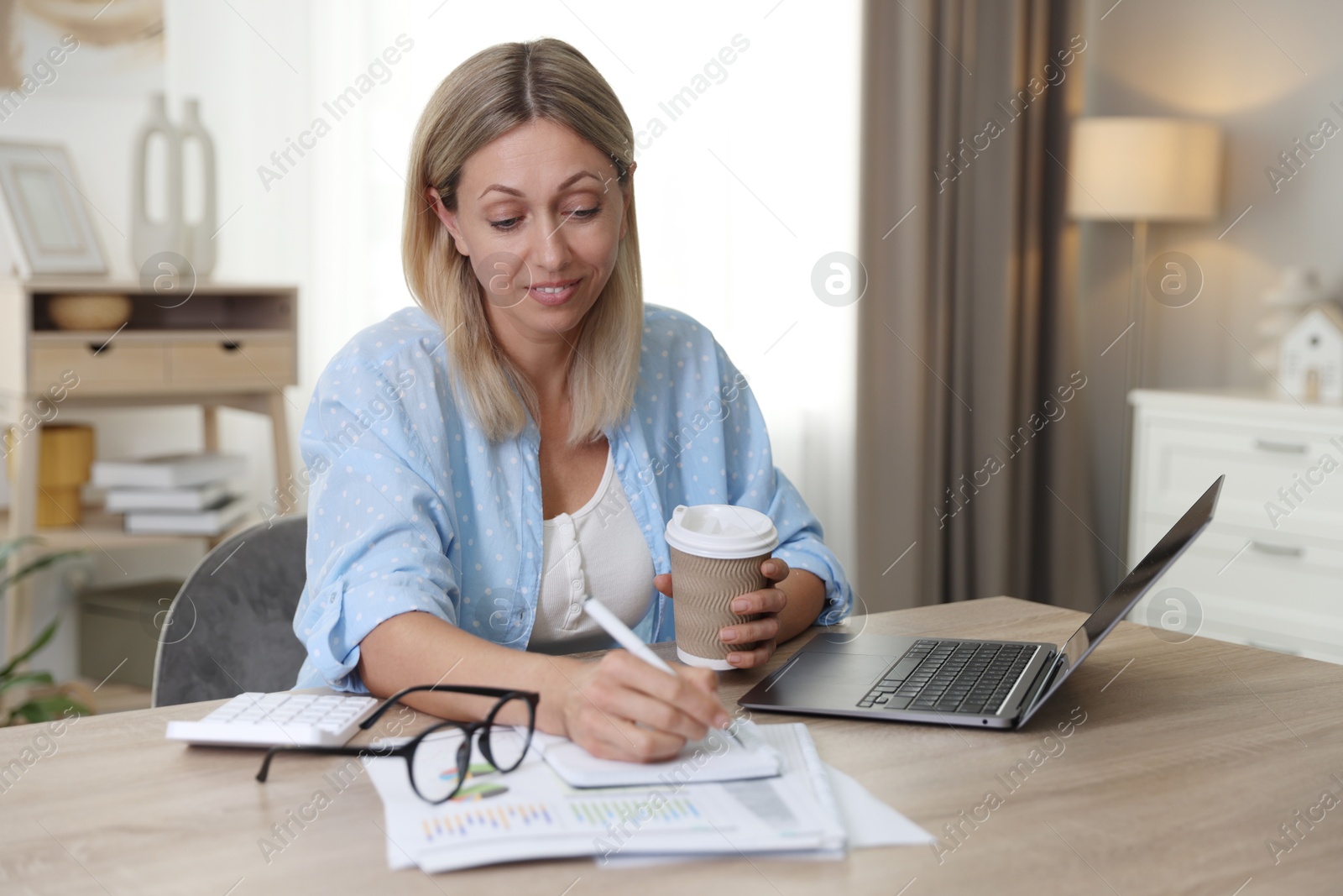 Photo of Budget planning. Woman with coffee taking notes at table indoors