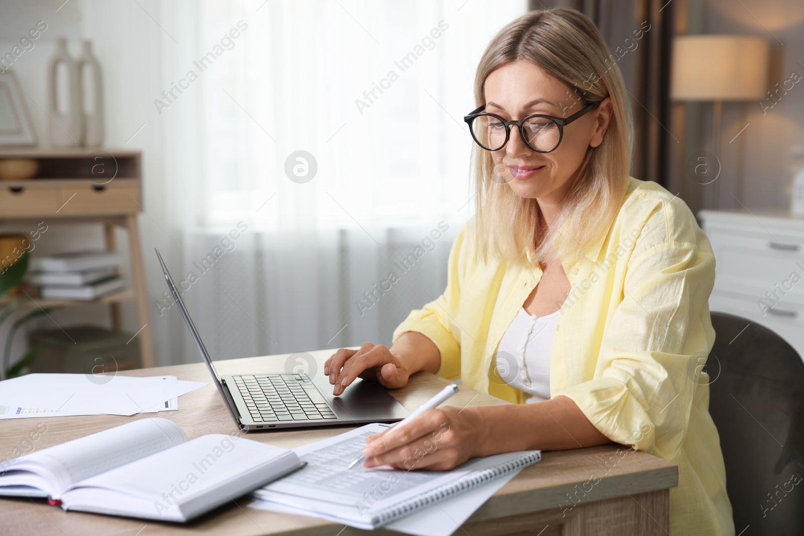 Photo of Budget planning. Woman using laptop while working with accounting documents at table indoors