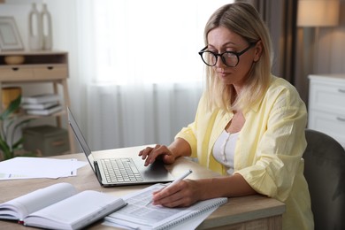 Photo of Budget planning. Woman using laptop while working with accounting documents at table indoors