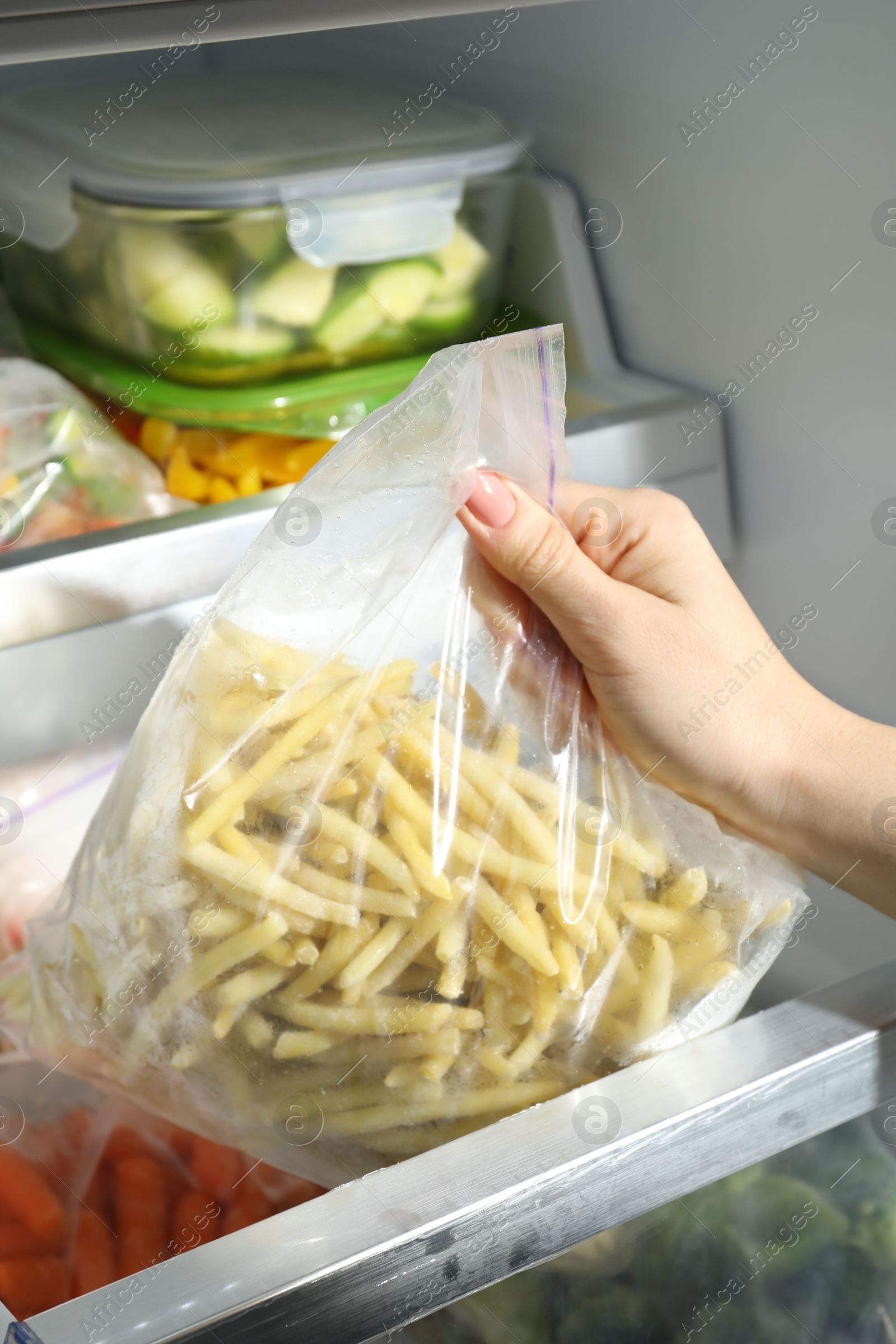 Photo of Woman taking plastic bag with frozen yellow beans from refrigerator, closeup