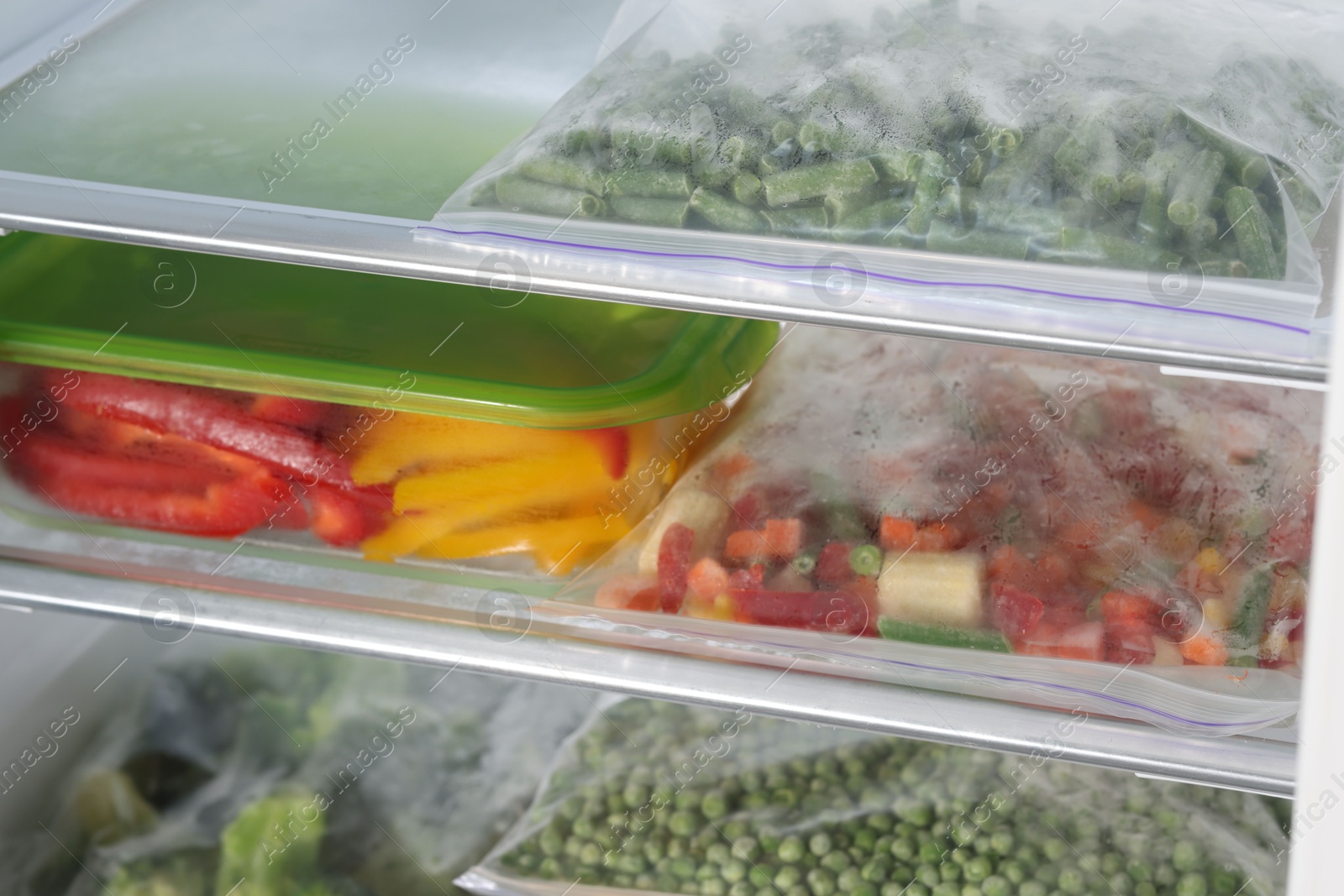 Photo of Plastic bags and glass container with different frozen vegetables in refrigerator, closeup