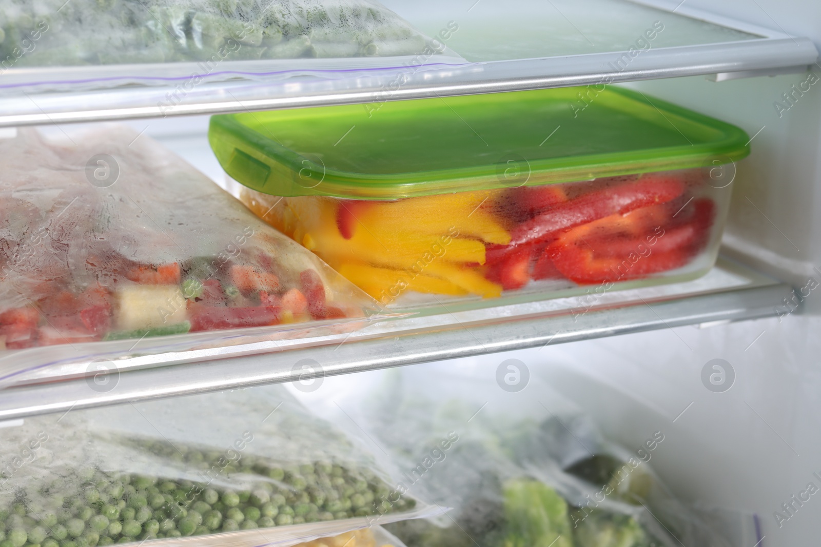 Photo of Plastic bags and glass container with different frozen vegetables in refrigerator, closeup