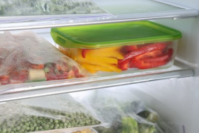 Photo of Plastic bags and glass container with different frozen vegetables in refrigerator, closeup